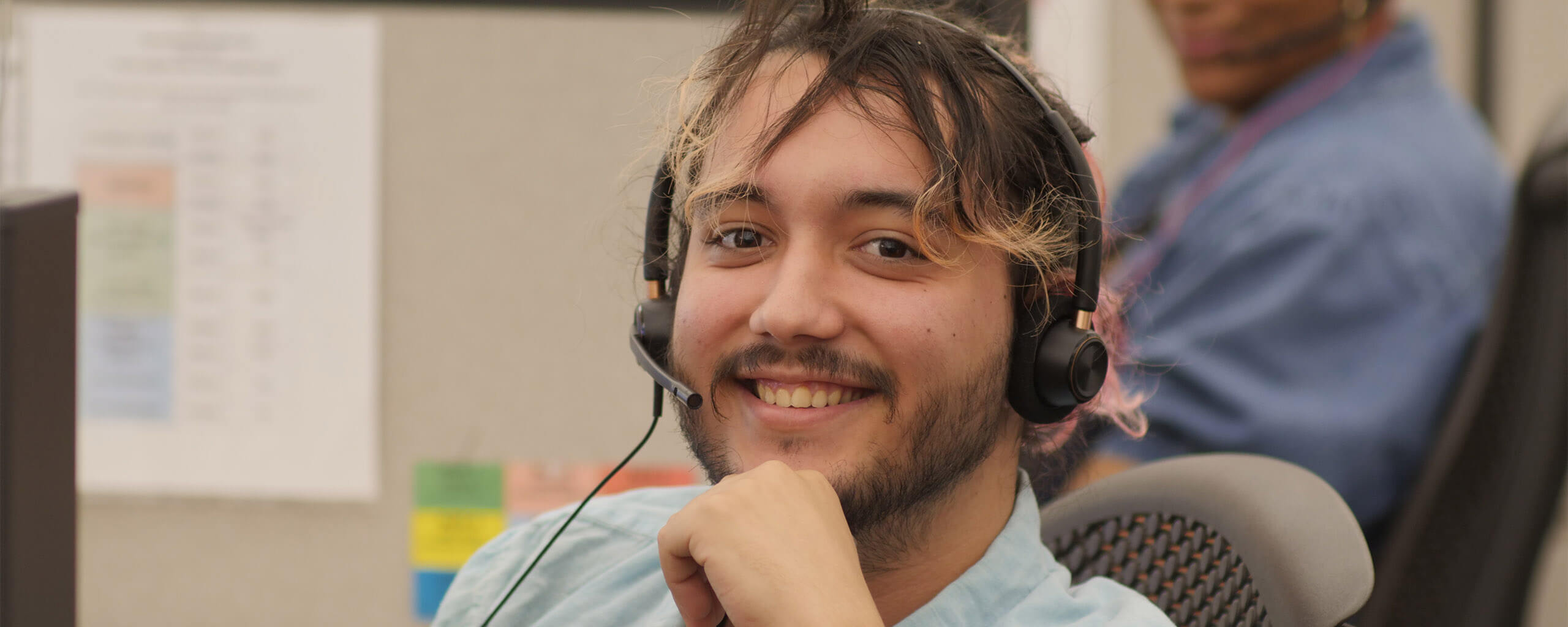 man smiling wearing a call center headset while sitting in an office chair