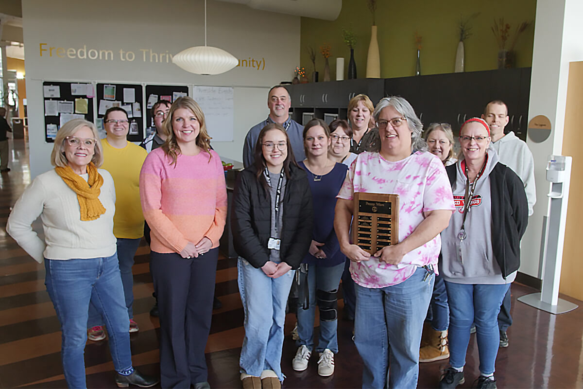 13 people standing in a group while one woman holds a plaque