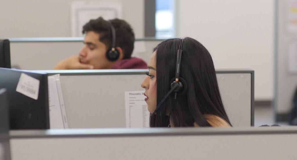 Two people working in cubicles wearing headsets